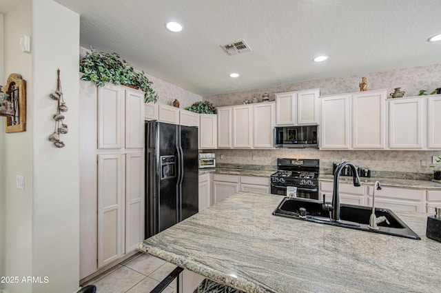 kitchen featuring visible vents, a sink, light tile patterned floors, light stone counters, and black appliances