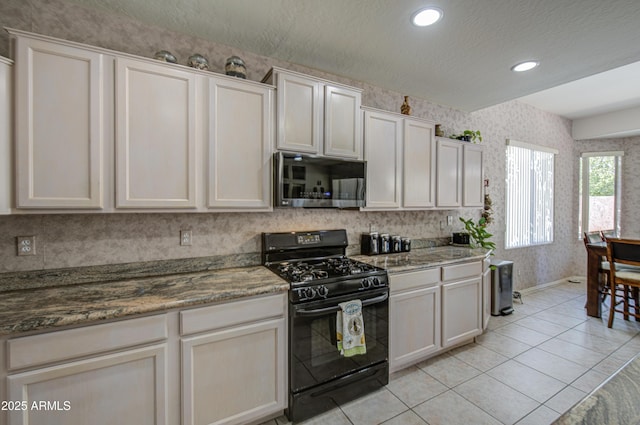 kitchen featuring baseboards, stainless steel microwave, black range with gas stovetop, wallpapered walls, and light tile patterned flooring