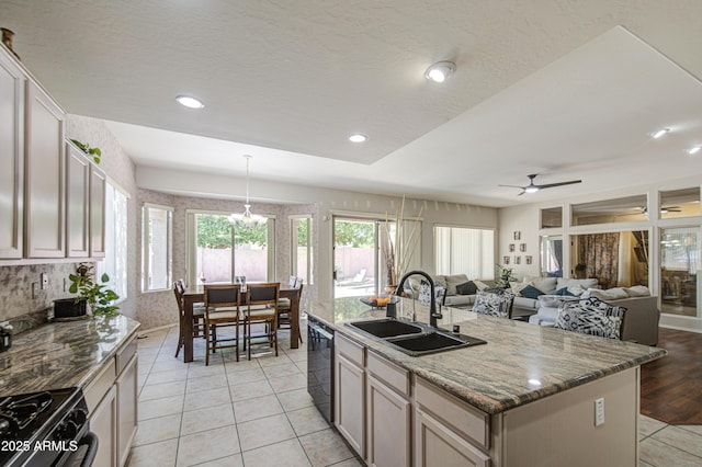 kitchen with light tile patterned flooring, a sink, ceiling fan with notable chandelier, a center island with sink, and black appliances