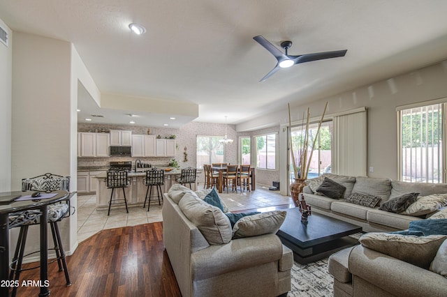 living area with light tile patterned floors, ceiling fan with notable chandelier, and recessed lighting