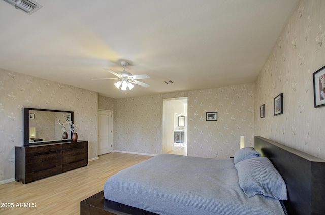 bedroom featuring a ceiling fan, wallpapered walls, visible vents, and wood finished floors