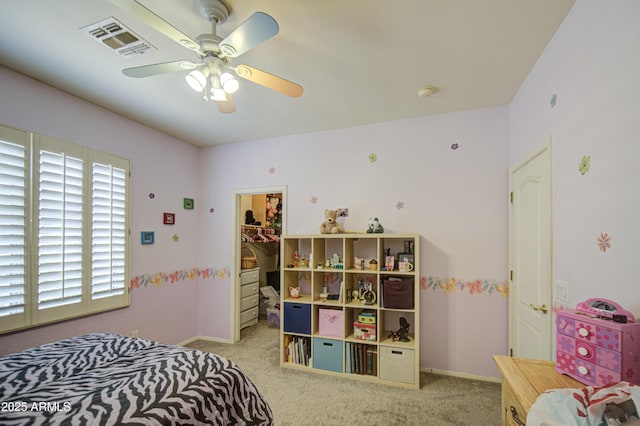 bedroom featuring a walk in closet, ceiling fan, visible vents, baseboards, and carpet