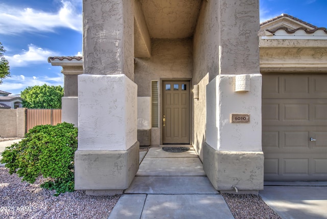 view of exterior entry with stucco siding, a tile roof, and fence