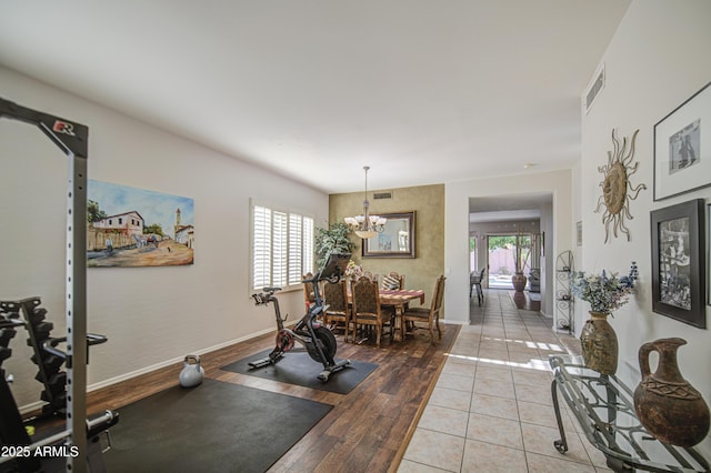 exercise area featuring baseboards, a notable chandelier, visible vents, and light wood-style floors