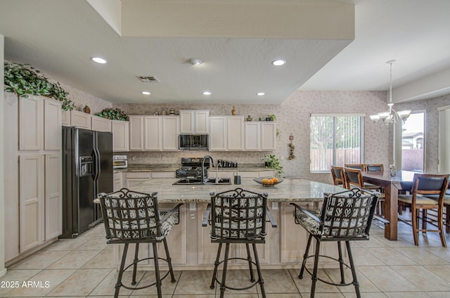 kitchen with light stone countertops, a sink, black refrigerator with ice dispenser, stainless steel microwave, and light tile patterned floors