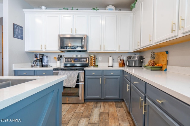 kitchen featuring white cabinets, gray cabinetry, appliances with stainless steel finishes, and light hardwood / wood-style flooring