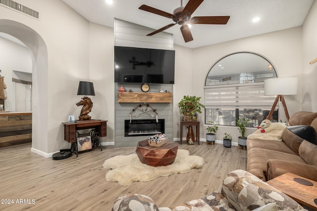 living room with ceiling fan, a fireplace, lofted ceiling, and light wood-type flooring