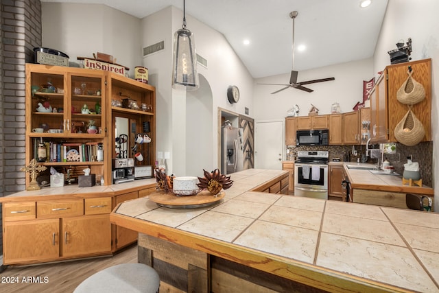 kitchen with tile countertops, tasteful backsplash, decorative light fixtures, light hardwood / wood-style floors, and stainless steel appliances