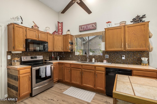 kitchen featuring decorative backsplash, light wood-type flooring, sink, black appliances, and tile counters