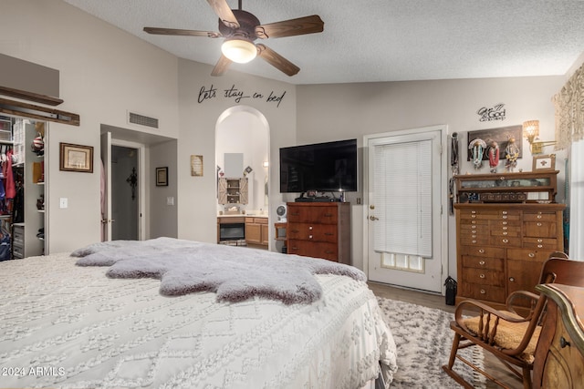 bedroom featuring ensuite bath, a textured ceiling, ceiling fan, high vaulted ceiling, and hardwood / wood-style floors