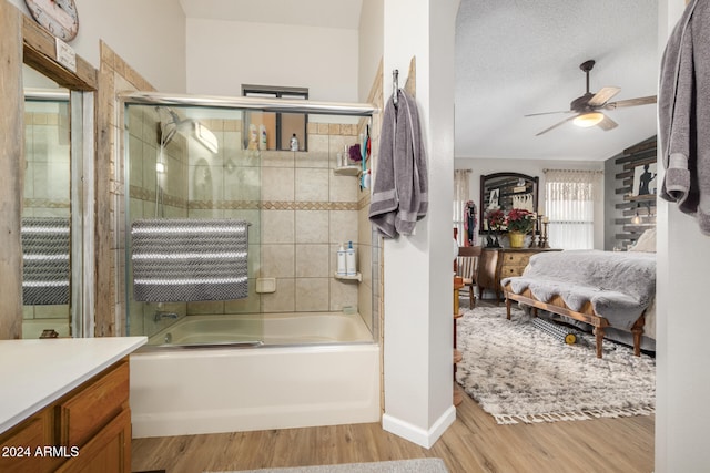 bathroom featuring hardwood / wood-style floors, vanity, bath / shower combo with glass door, ceiling fan, and a textured ceiling