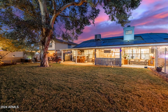 back house at dusk featuring a lawn, a patio area, and solar panels