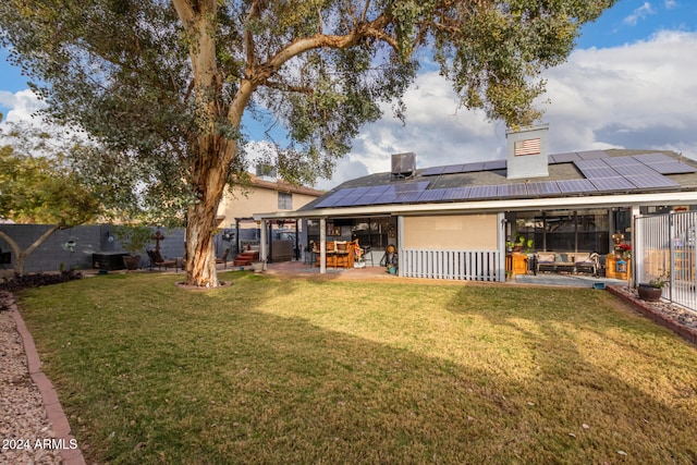 rear view of property featuring a lawn, a patio area, and solar panels