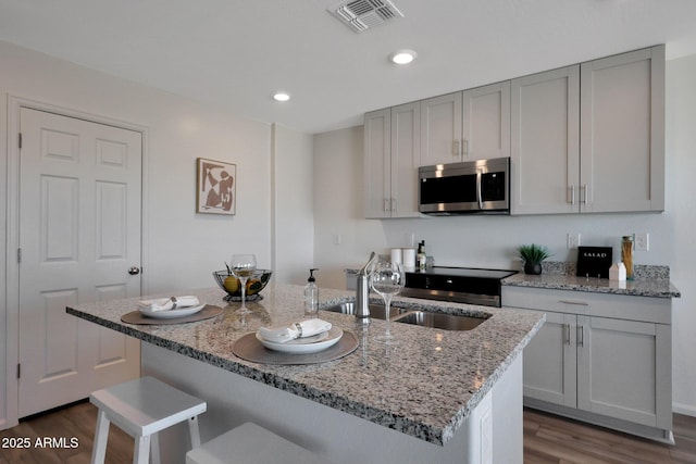 1234 N 13th St, Coolidge, AZ 85128 - kitchen with stainless steel microwave, dark wood-style floors, gray cabinetry, light stone countertops, and a center island with sink