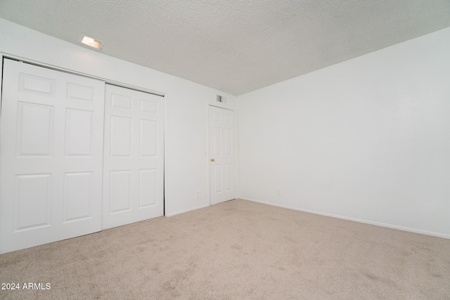 unfurnished bedroom with light carpet, a textured ceiling, and a closet