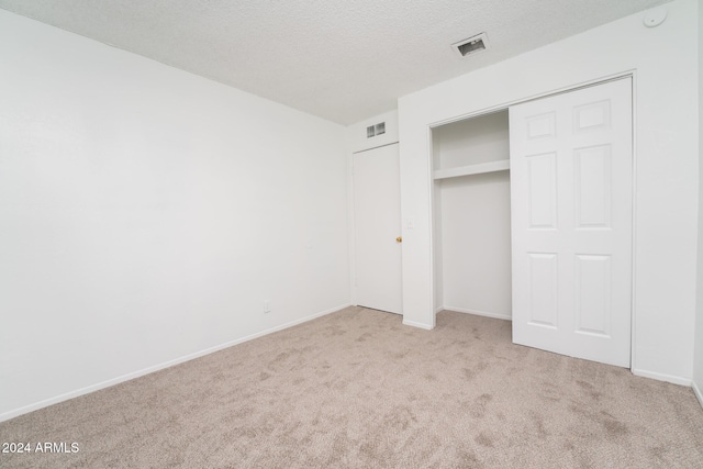 unfurnished bedroom featuring a textured ceiling, light colored carpet, and a closet