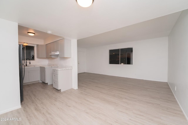 kitchen with black fridge, sink, light wood-type flooring, gray cabinets, and light stone counters