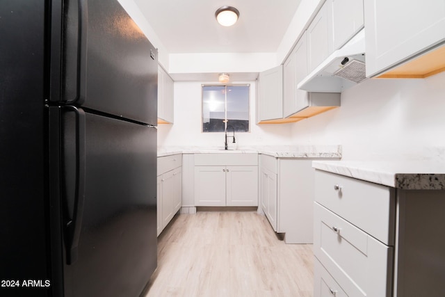 kitchen with white cabinetry, black refrigerator, range hood, light hardwood / wood-style floors, and sink