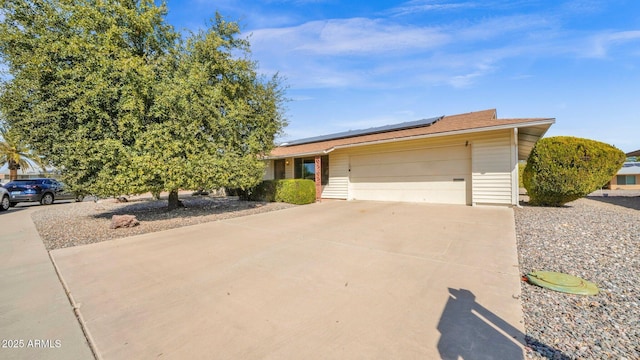 single story home featuring a garage, solar panels, and concrete driveway