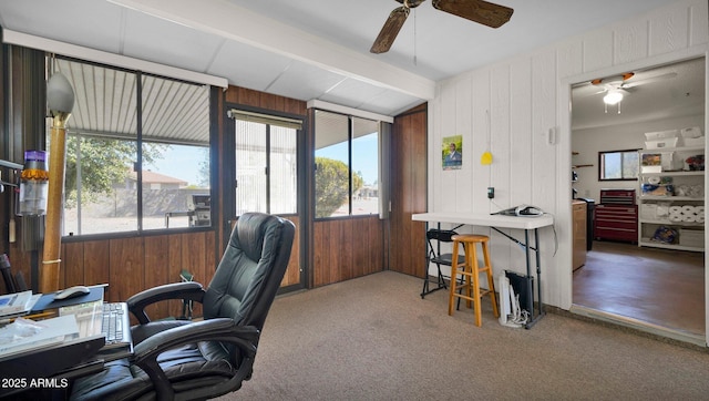 carpeted home office with lofted ceiling with beams, wood walls, and a ceiling fan