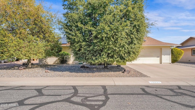 view of property hidden behind natural elements with a garage and concrete driveway