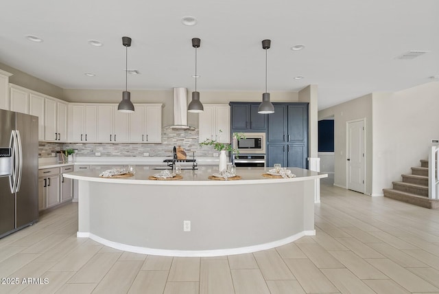 kitchen with backsplash, an island with sink, light countertops, appliances with stainless steel finishes, and wall chimney exhaust hood