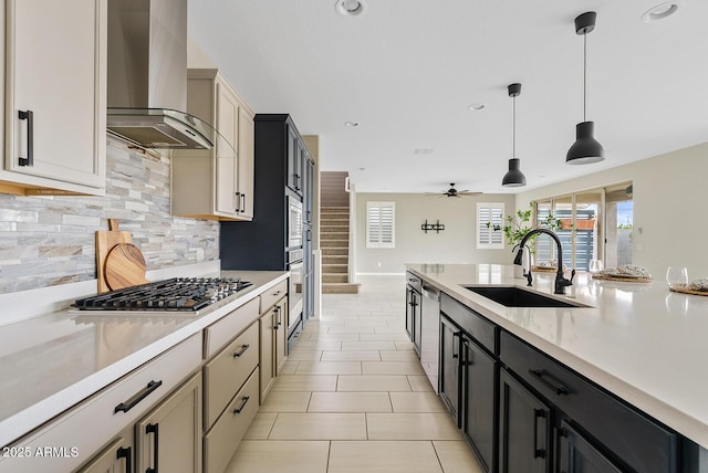 kitchen with backsplash, light countertops, stainless steel appliances, wall chimney exhaust hood, and a sink