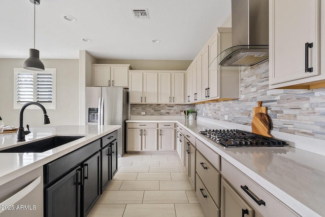 kitchen featuring visible vents, a sink, wall chimney range hood, appliances with stainless steel finishes, and light countertops