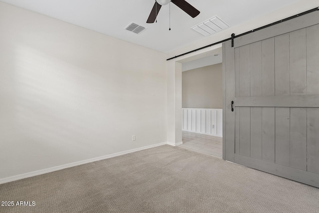 unfurnished room featuring a barn door, visible vents, ceiling fan, and carpet flooring