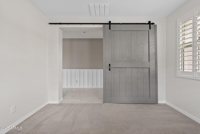 carpeted empty room with visible vents, a barn door, and baseboards