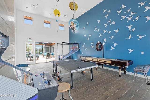 recreation room with visible vents, a towering ceiling, baseboards, and wood finished floors