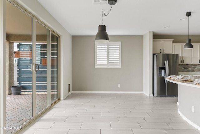 interior space featuring decorative backsplash, baseboards, pendant lighting, and stainless steel fridge with ice dispenser