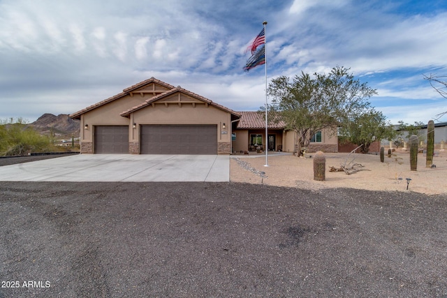 view of front of house featuring concrete driveway, stone siding, a tile roof, an attached garage, and stucco siding