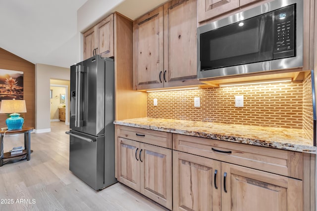 kitchen with built in microwave, high end fridge, decorative backsplash, light brown cabinetry, and light wood-type flooring