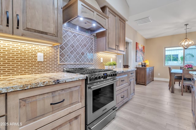 kitchen with light stone counters, high end stove, premium range hood, visible vents, and tasteful backsplash