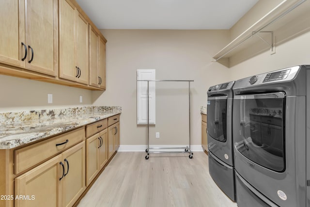 laundry area featuring light wood-type flooring, cabinet space, baseboards, and separate washer and dryer