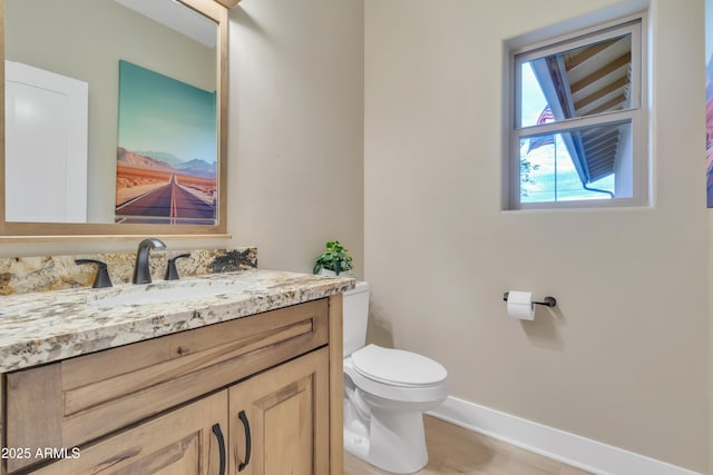 half bath with toilet, baseboards, and vanity