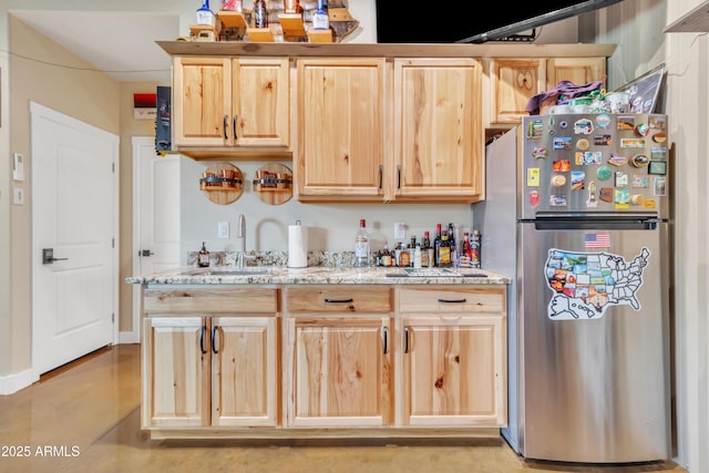 kitchen with light stone countertops, light brown cabinetry, a sink, and freestanding refrigerator