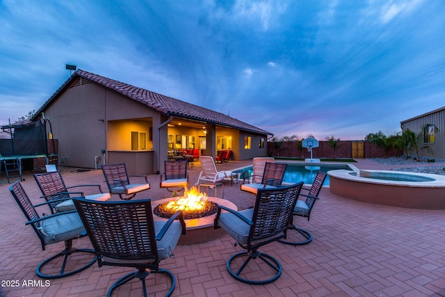 view of patio / terrace with a fire pit, a fenced in pool, an in ground hot tub, a trampoline, and fence