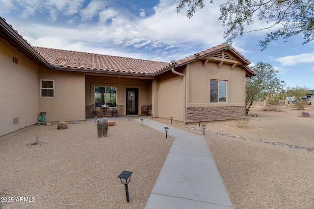 view of front of home featuring stone siding, a patio area, a tile roof, and stucco siding