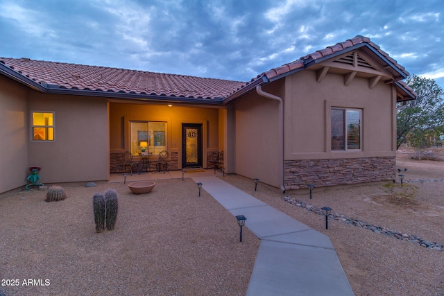 back of property with stone siding, a tiled roof, stucco siding, and a patio