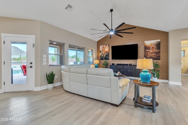 living room featuring vaulted ceiling, light wood finished floors, visible vents, and baseboards