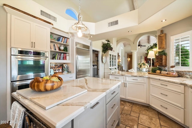 kitchen with a center island, light stone counters, pendant lighting, white cabinets, and appliances with stainless steel finishes