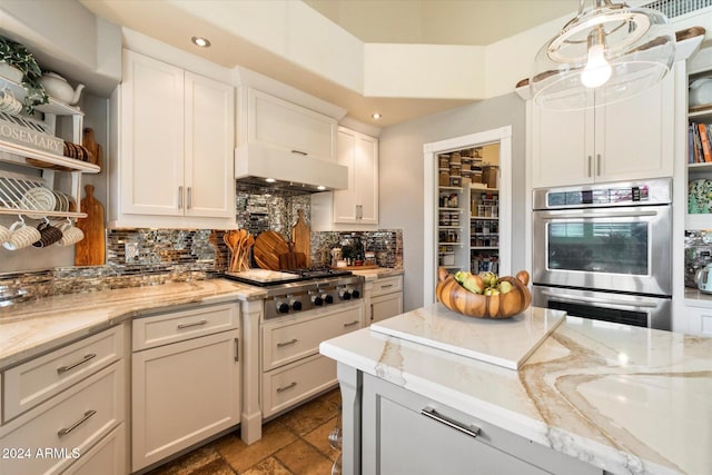 kitchen featuring light stone countertops, range hood, tasteful backsplash, decorative light fixtures, and stainless steel appliances