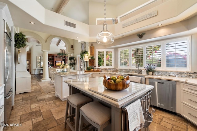 kitchen with appliances with stainless steel finishes, a towering ceiling, decorative columns, white cabinets, and a kitchen island