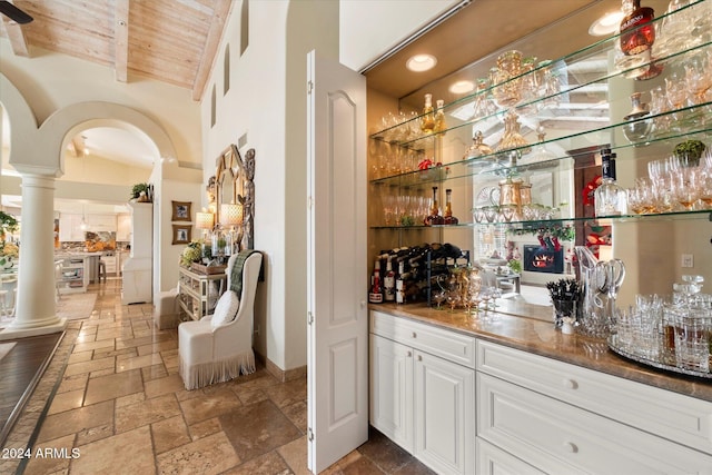 bar with white cabinetry, high vaulted ceiling, and decorative columns