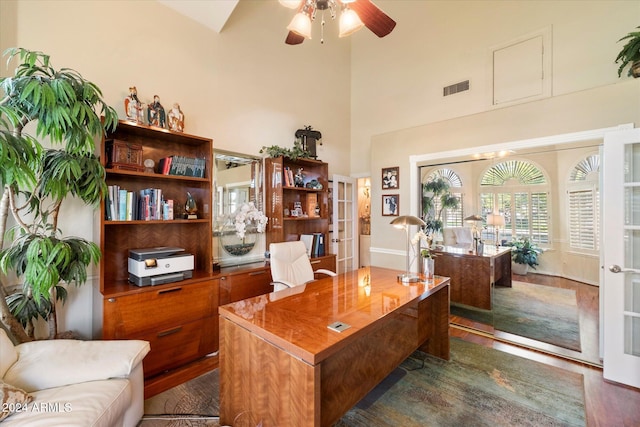 home office featuring dark hardwood / wood-style floors, ceiling fan, a towering ceiling, and french doors