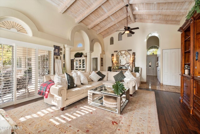 living room featuring ceiling fan, dark hardwood / wood-style flooring, high vaulted ceiling, beamed ceiling, and decorative columns