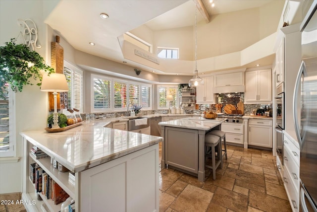 kitchen with pendant lighting, kitchen peninsula, light stone counters, a kitchen bar, and white cabinetry