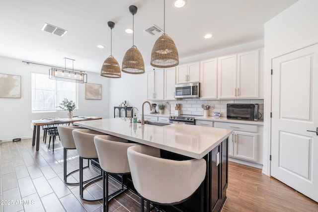 kitchen with stainless steel appliances, decorative light fixtures, white cabinetry, and a kitchen island with sink